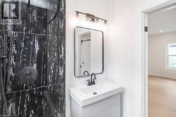 Bathroom featuring black-and-white tiled shower, wall-mounted vanity with integrated sink, black framed mirror, and a three-light fixture - 