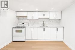 Kitchenette with light wood-finish flooring, white cabinetry, integrated stainless steel sink, and a white range - 