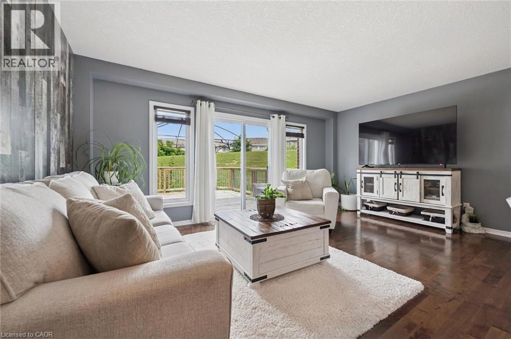 Dark wood-finish flooring, accent wall with wood paneling, sliding glass door with deck access, built-in entertainment console, and neutral wall paint - 308 Parkvale Drive, Kitchener, ON - Indoor Photo Showing Living Room