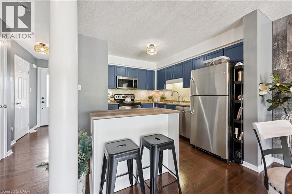 Kitchen featuring blue cabinetry, stainless steel appliances, a wood-finish breakfast bar, and wood-finish flooring - 308 Parkvale Drive, Kitchener, ON - Indoor Photo Showing Kitchen