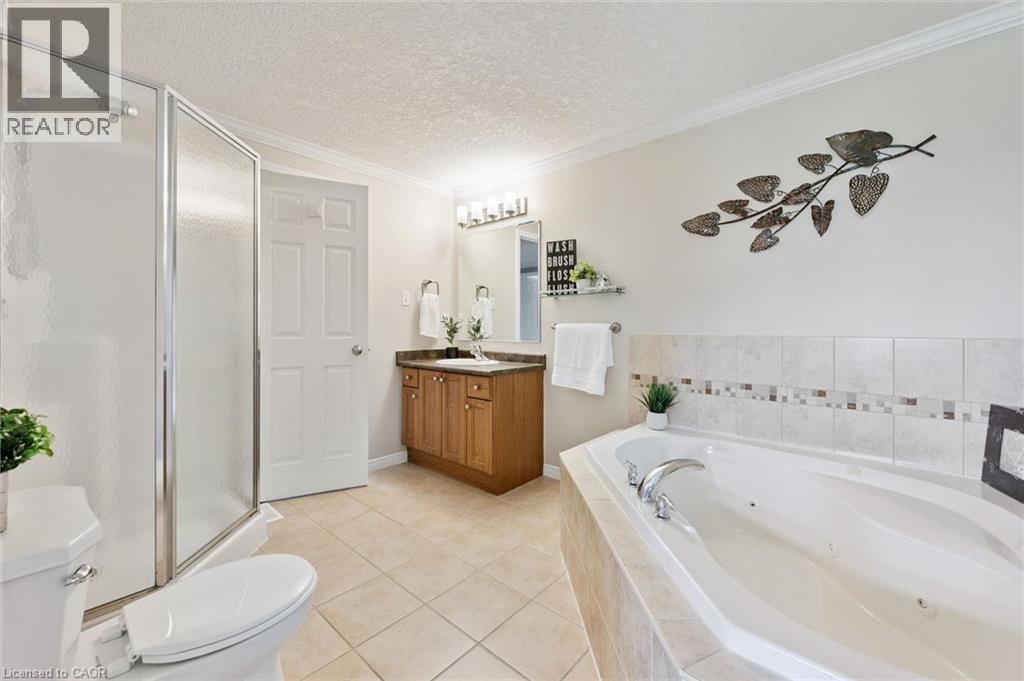 Tiled flooring, built-in soaking tub, wood-finish vanity with countertop, framed mirror, and glass-enclosed shower - 308 Parkvale Drive, Kitchener, ON - Indoor Photo Showing Bathroom