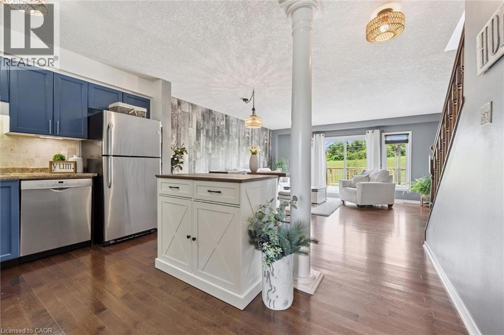 Wood-finish flooring throughout, kitchen with blue cabinetry and stainless steel appliances, white freestanding kitchen island with a wood-finish top, and a living area with sliding glass doors - 308 Parkvale Drive, Kitchener, ON - Indoor Photo Showing Kitchen