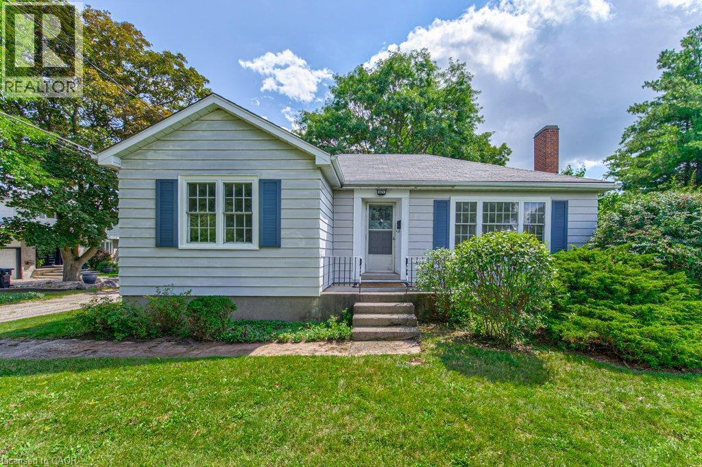 Siding exterior with blue window shutters, front entry with steps and railing, brick chimney, and mature landscaping - 321 Highland Park, Cambridge, ON
