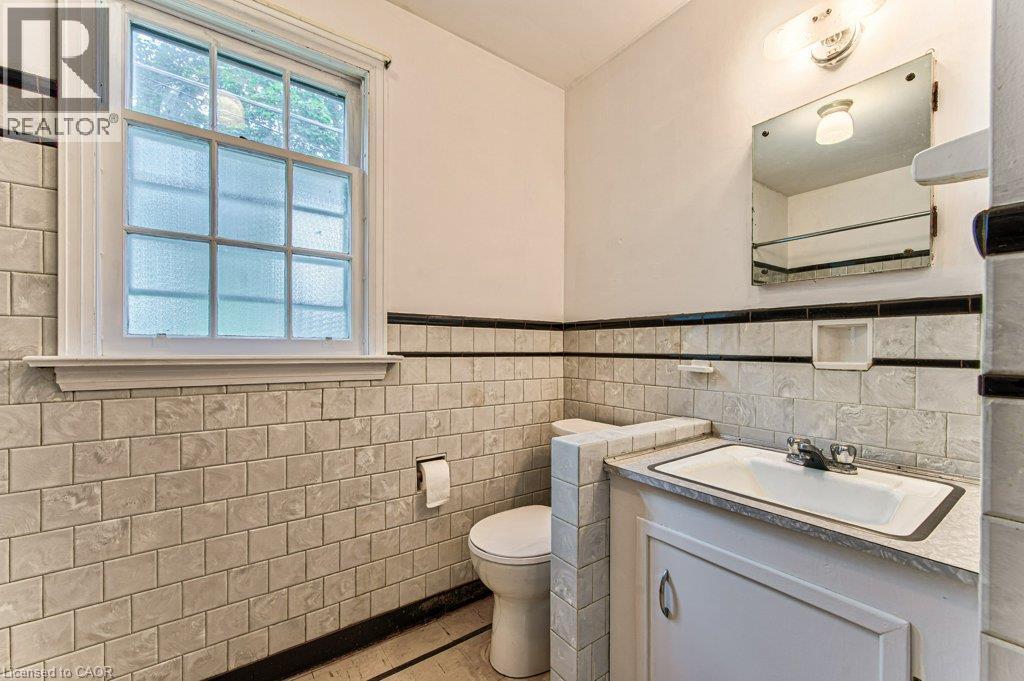 Built-in vanity with integrated sink, wall-mounted mirror, and tile wainscoting with a dark accent border - 321 Highland Park, Cambridge, ON