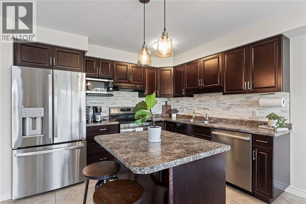 Kitchen featuring dark wood-finish cabinetry, stainless steel appliances, a center island with seating, pendant lighting, and a tile backsplash - 783 Frontenac Crescent, Woodstock, ON - Indoor Photo Showing Kitchen With Double Sink