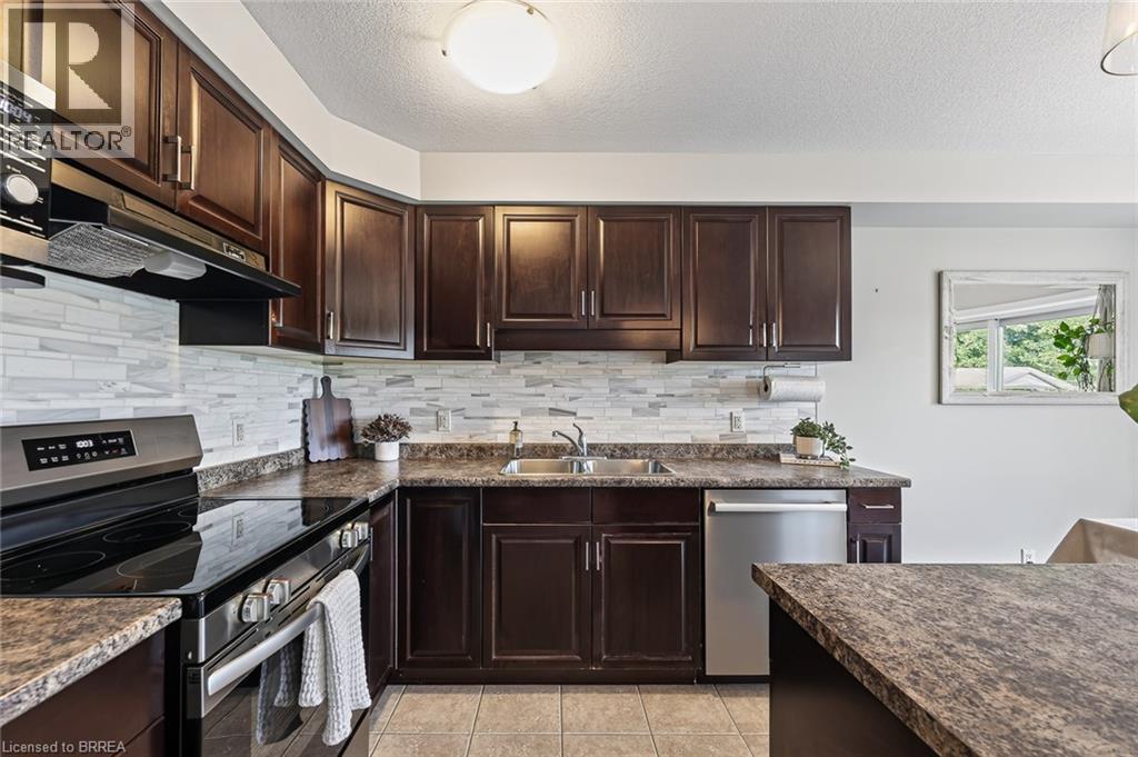 Dark wood-finish cabinetry with stainless steel hardware, mosaic tile backsplash, stainless steel appliances, and a double basin sink - 783 Frontenac Crescent, Woodstock, ON - Indoor Photo Showing Kitchen With Double Sink