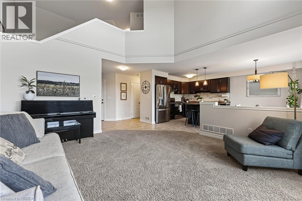Carpeted living area with high ceilings, recessed lighting, and a partial wall separating a kitchen with dark cabinetry and stainless steel appliances - 783 Frontenac Crescent, Woodstock, ON - Indoor Photo Showing Living Room