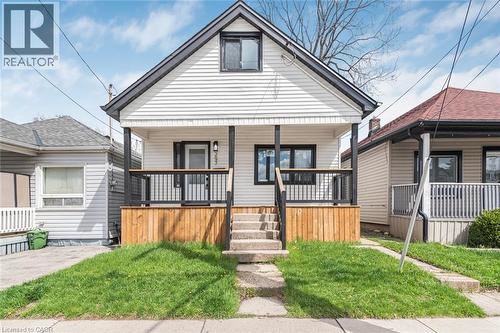 Gable-roof property featuring white horizontal siding, black trim accents, a covered front porch with a wood-paneled base, black railings, and concrete steps - 297 Britannia Avenue, Hamilton, ON - Outdoor With Deck Patio Veranda