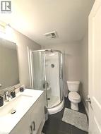Curved glass shower enclosure, single-basin vanity, stainless steel faucet, and dark tile flooring - 