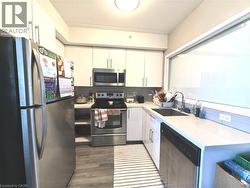 Modern kitchen featuring stainless steel appliances, light-toned cabinetry, wood-finish flooring, a contemporary sink, and a large horizontal window - 