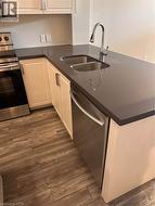 Kitchen featuring wood-finish flooring, white cabinetry, dark countertops, a double basin sink with a chrome faucet, and stainless steel appliances including a dishwasher and range - 