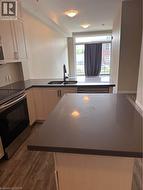 Kitchen featuring white cabinetry, dark countertops, wood-finish flooring, stainless steel appliances, and a built-in sink with a black faucet - 