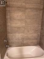 Spa-inspired bathroom featuring tile surround in warm wood-finish tones, chrome fixtures, and a freestanding soaking tub with clean lines and modern styling - 
