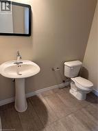 Pedestal sink with chrome faucet, wall-mounted mirror, white toilet, and wood-finish tile flooring - 