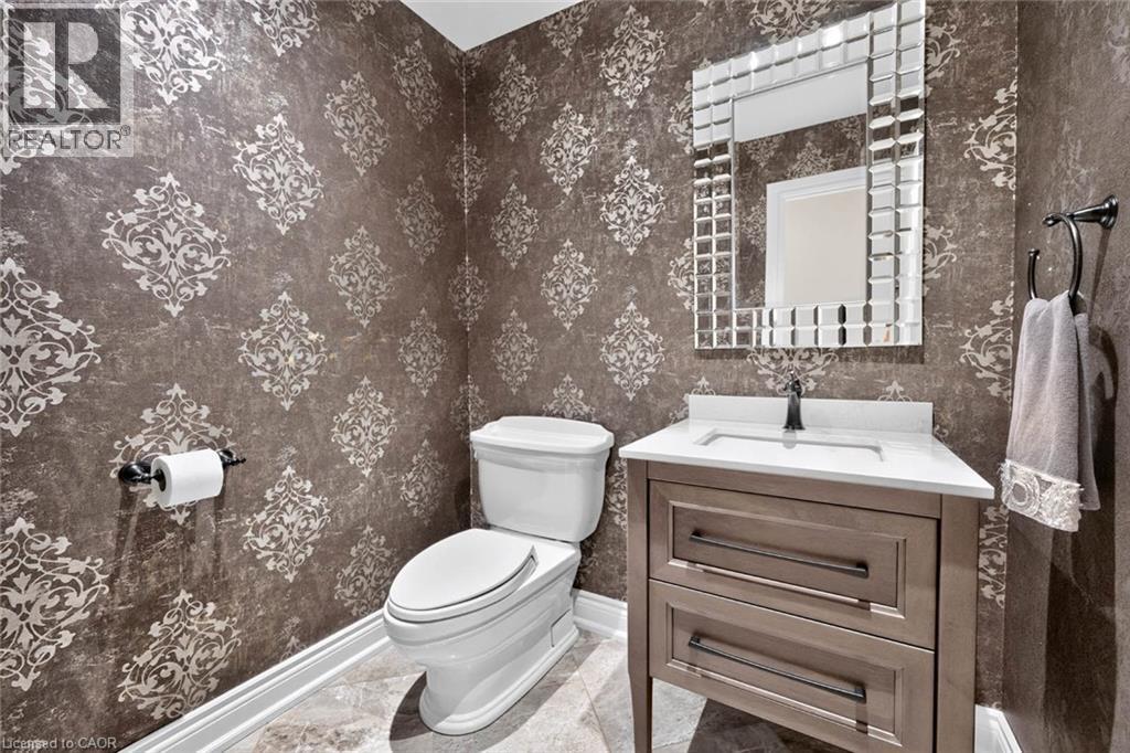 Damask-patterned walls with a wood-finish vanity, white countertop, and a tiled mirror frame - 11 Christman Court, Markham, ON - Indoor Photo Showing Bathroom