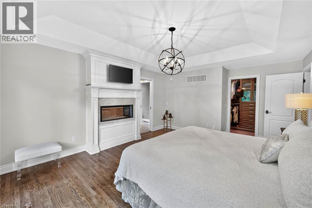 Tray ceiling with a spherical chandelier, wood-finish flooring, white mantel, built-in fireplace, and an open closet with built-in shelving - 11 Christman Court, Markham, ON - Indoor Photo Showing Bedroom