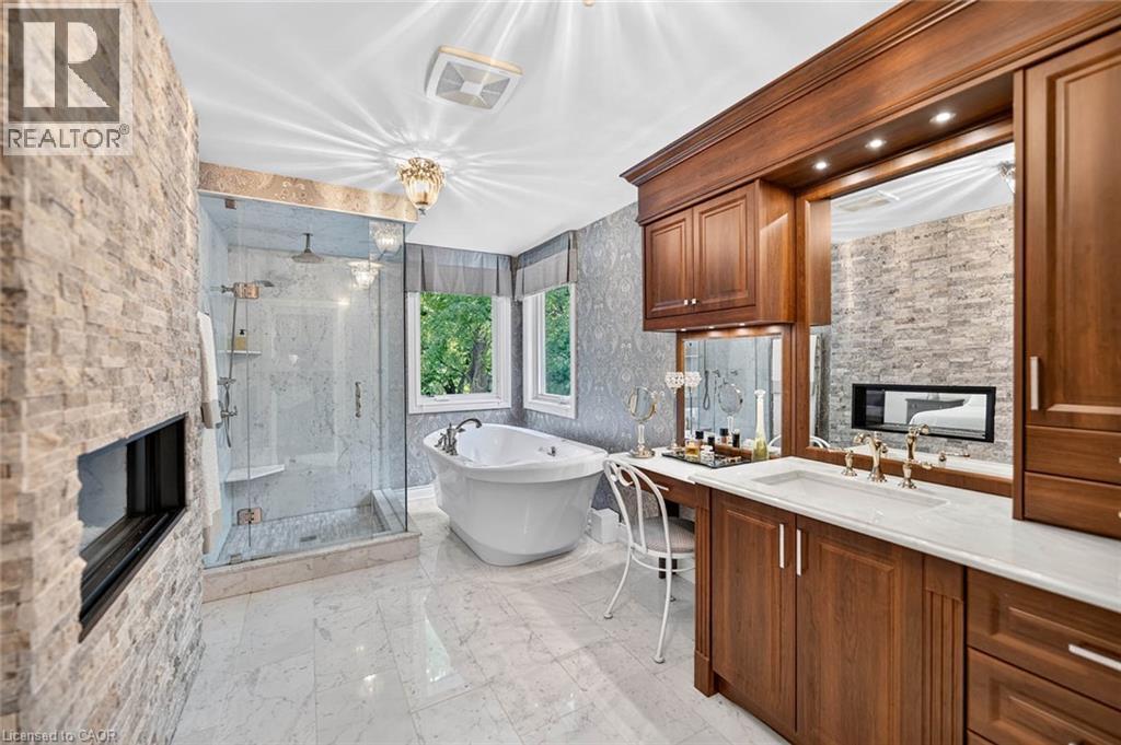 Spacious bathroom featuring a freestanding tub, glass-enclosed shower, stone accent wall with built-in fireplace, and a wood-finish vanity with countertop sink - 11 Christman Court, Markham, ON - Indoor Photo Showing Other Room