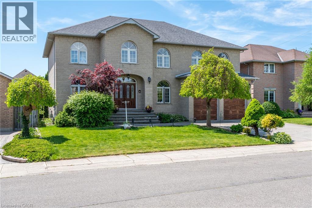 Brick exterior with multiple arched windows, a double-door entry, a two-car garage with wood-finish doors, and a paved driveway - 23 Susan Drive, Hamilton, ON