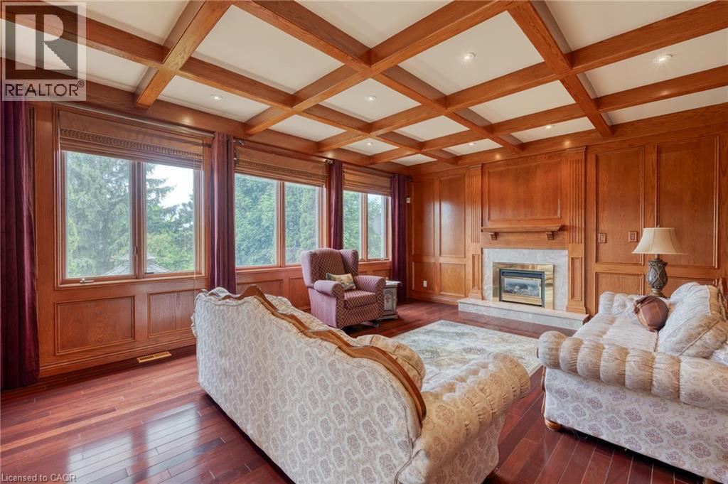 Coffered ceiling with recessed lighting, rich wood paneling, multiple large windows, wood-finish flooring, and a fireplace with a stone surround and wood mantel - 23 Susan Drive, Hamilton, ON