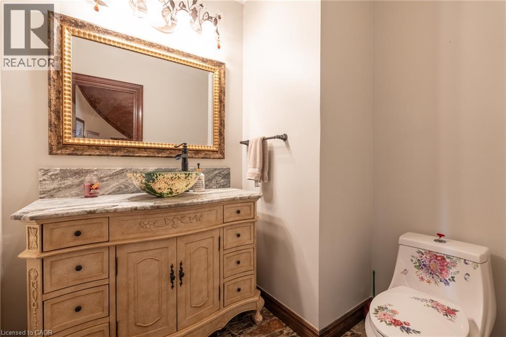 Vanity with a vessel sink, decorative mirror, stone countertop, and a patterned toilet - 23 Susan Drive, Hamilton, ON