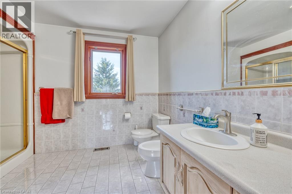 Bathroom featuring tile flooring, a built-in vanity with a countertop and undermount sink, a framed mirror, a window with wood trim, and a shower with a gold-toned frame - 23 Susan Drive, Hamilton, ON
