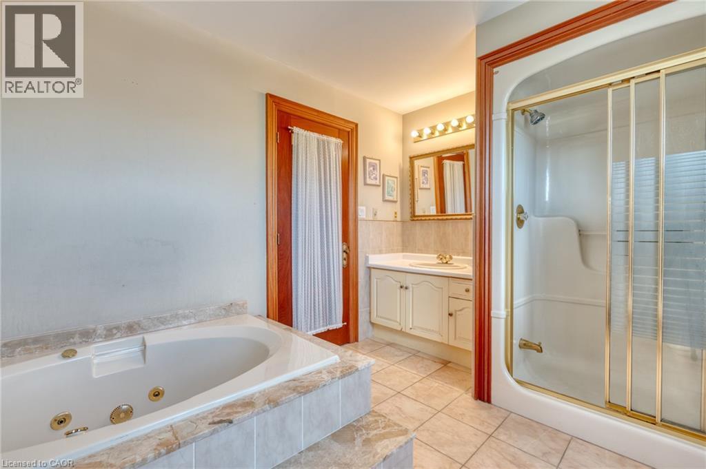 Jetted tub with tiled surround, separate shower with sliding glass doors, single vanity with integrated sink, and tile flooring - 23 Susan Drive, Hamilton, ON