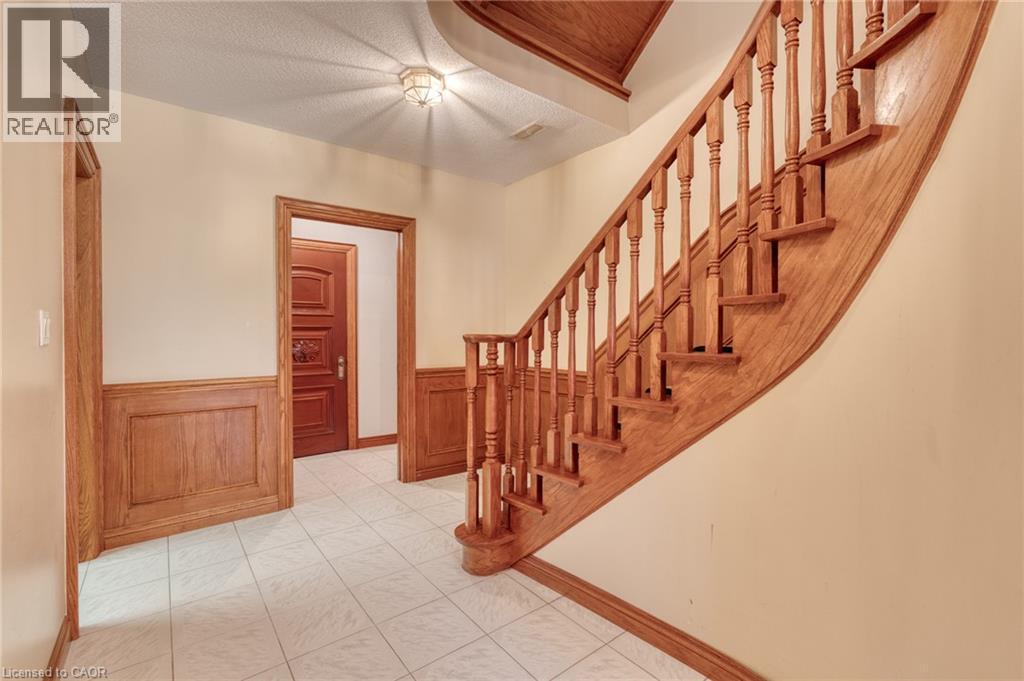 Curved wood staircase with turned balusters, wood paneling, wood door frames, wood paneled doors, and square tile flooring - 23 Susan Drive, Hamilton, ON