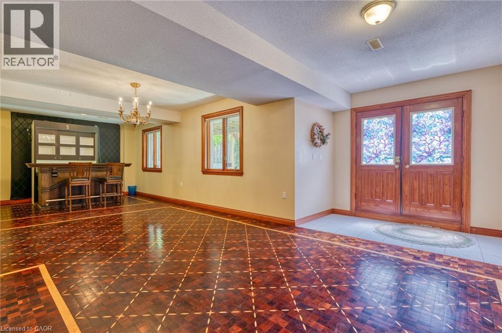 Spacious open-concept entertaining area featuring rich wood-finish flooring with geometric inlay detailing, decorative crown molding, and recessed ceiling lighting - 23 Susan Drive, Hamilton, ON