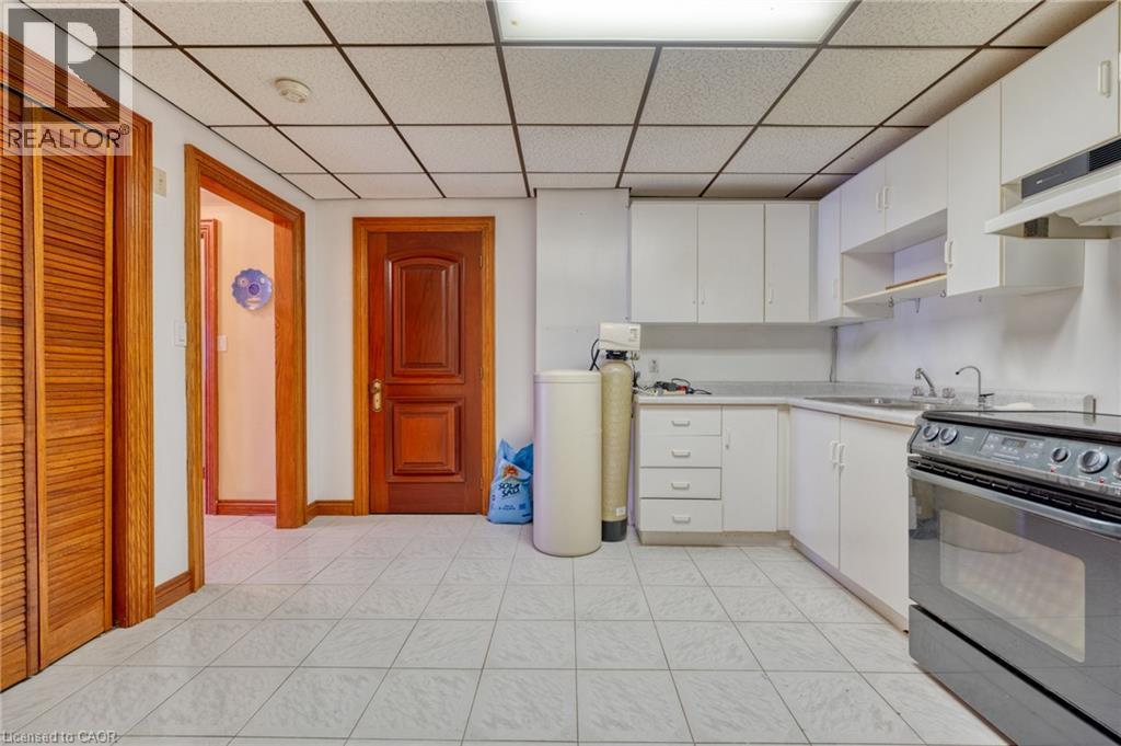 Spacious kitchen featuring stainless steel gas range with double ovens, white cabinetry with open shelving, tile flooring throughout, and multiple entry points - 23 Susan Drive, Hamilton, ON