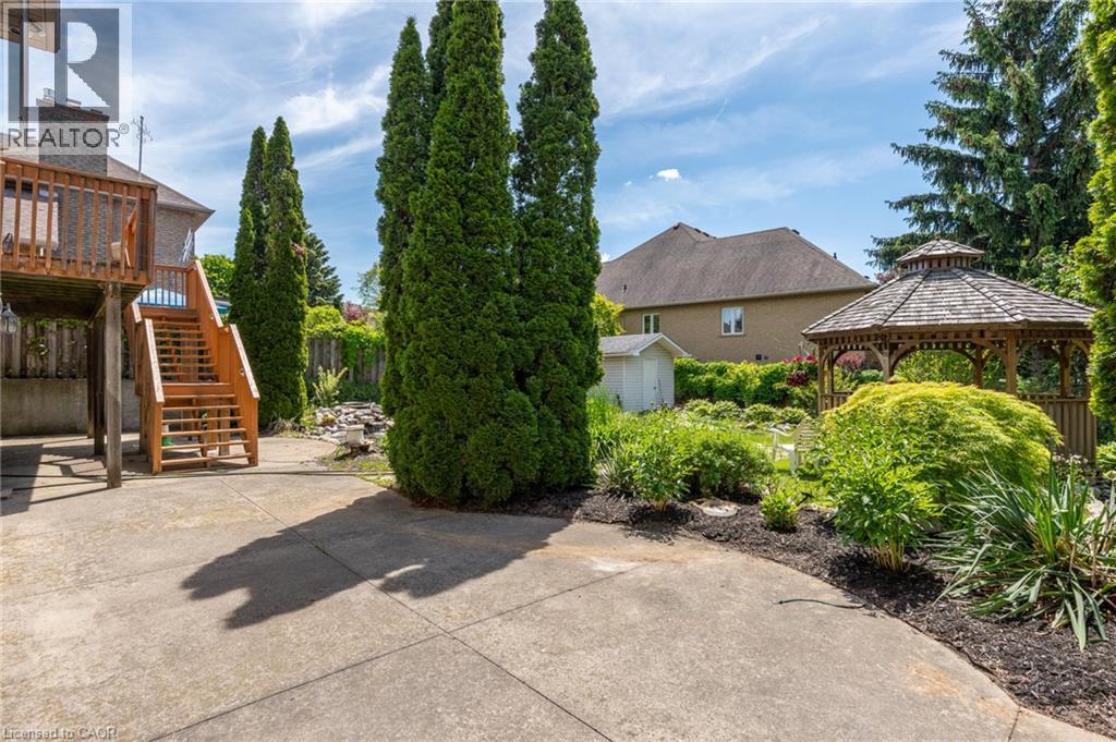 Expansive concrete patio with a wooden deck and stairs, surrounded by mature trees, a garden gazebo, and lush landscaping - 23 Susan Drive, Hamilton, ON