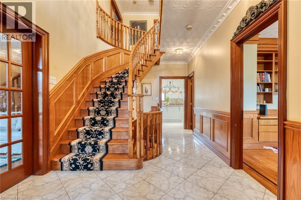 Grand entryway featuring a curved wood staircase with a decorative runner, marble-finish tile flooring, wood paneling, and a built-in wood-finish shelving unit - 23 Susan Drive, Hamilton, ON