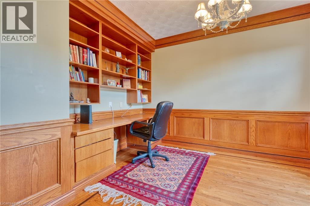 Sophisticated home office featuring rich wood cabinetry with integrated desk workspace, built-in shelving for extensive book storage, wainscoting detail, hardwood flooring, and a professional ergonomi - 23 Susan Drive, Hamilton, ON