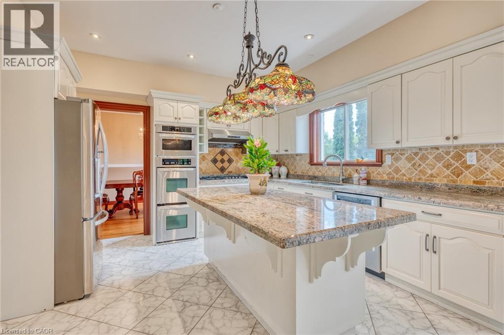 Kitchen featuring white cabinetry, stone countertops, a tiled backsplash, built-in stainless steel appliances, and a central island - 23 Susan Drive, Hamilton, ON