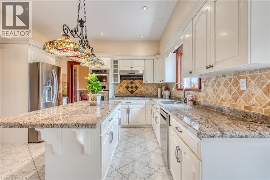 Kitchen featuring an expansive island with stone countertops, white cabinetry, tile flooring, a tile backsplash, and stainless steel appliances - 23 Susan Drive, Hamilton, ON