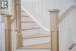 Open staircase featuring light wood-finish treads, white risers, and a coordinated wood-finish newel post and handrail - 
