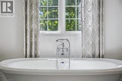 Freestanding soaking tub with polished chrome fixtures, white window trim, and patterned drapes - 