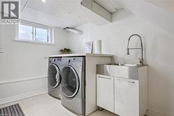 Laundry area featuring a stainless steel utility sink with a coiled spring faucet, white cabinetry, and a drop-panel ceiling - 