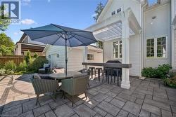 Expansive paver patio with a pergola-covered outdoor kitchen, built-in bar, and white siding exterior - 