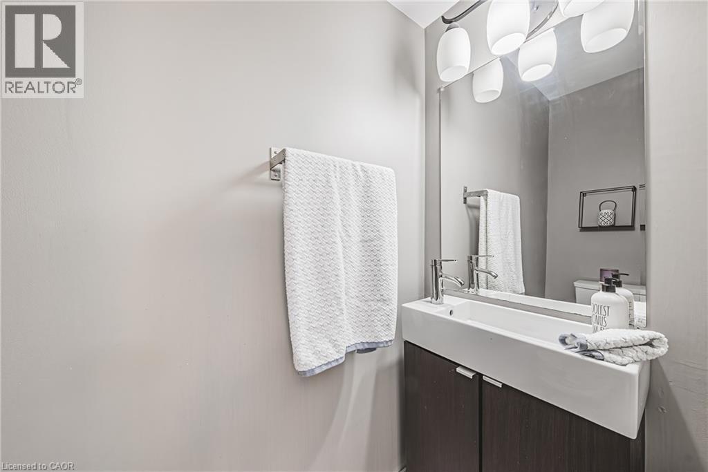 Vanity with an integrated rectangular sink, wood-finish cabinetry, chrome fixtures, and a mirrored wall - 266 Limeridge Road E Unit# 3, Hamilton, ON