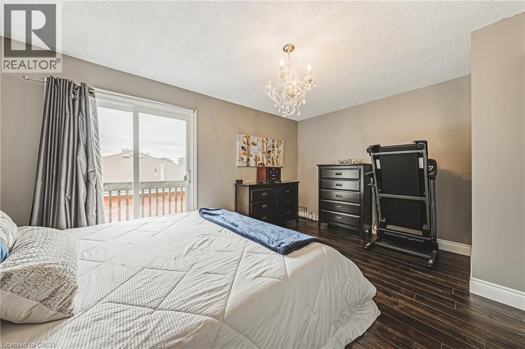Sliding glass door opening to a private balcony with wood railing, dark wood-finish flooring, and a crystal chandelier - 266 Limeridge Road E Unit# 3, Hamilton, ON