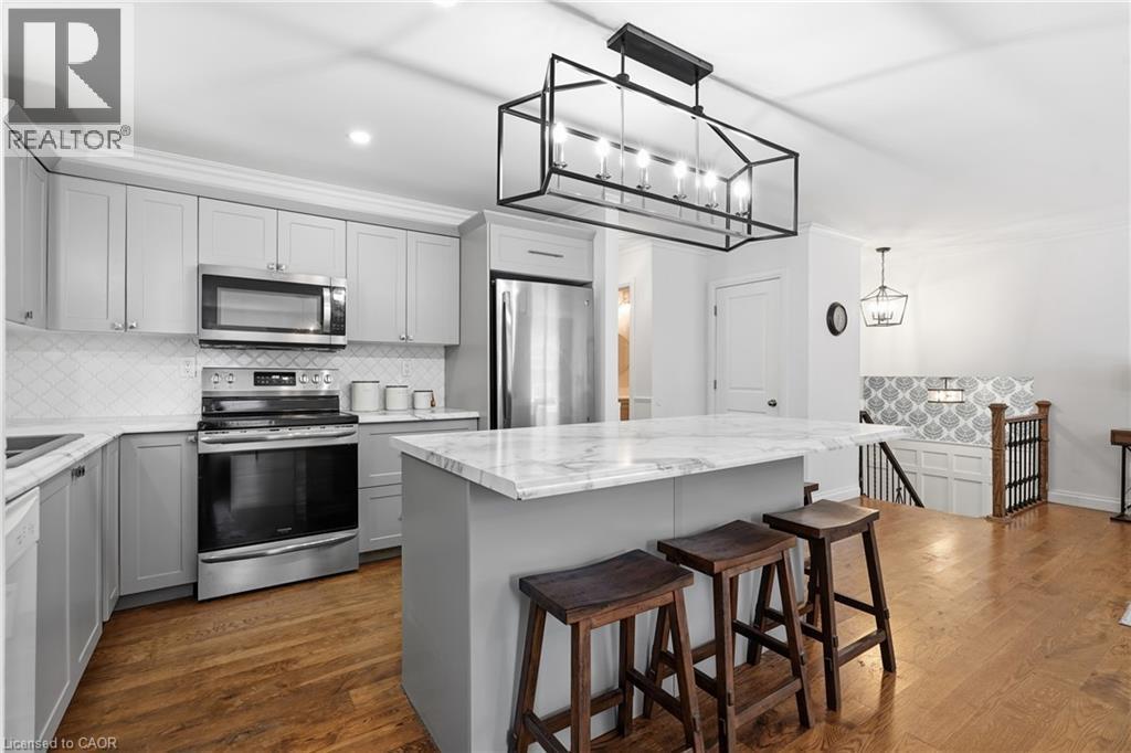 Kitchen featuring light gray cabinetry, stainless steel appliances, a white patterned tile backsplash, and wood-finish flooring - 72 Crestlynn Crescent, Simcoe, ON