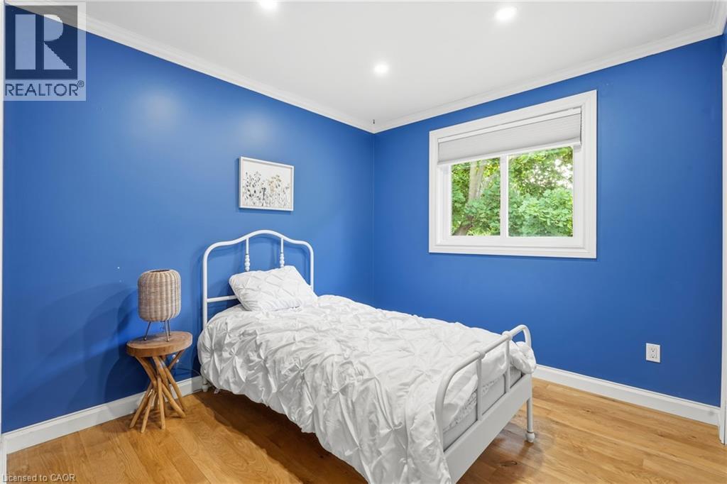 Bedroom featuring vibrant blue walls, white trim, wood-finish flooring, and a window with a roller shade - 72 Crestlynn Crescent, Simcoe, ON