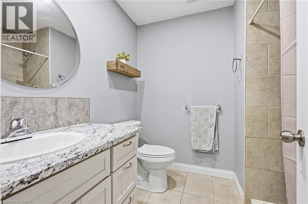 Bathroom featuring a white vanity with a patterned countertop, circular mirror, and tile flooring - 72 Crestlynn Crescent, Simcoe, ON