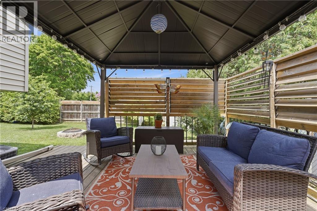 Expansive outdoor deck featuring a dark metal gazebo with string lighting, wood-finish slatted privacy screens, and a natural wood-finish deck surface - 72 Crestlynn Crescent, Simcoe, ON