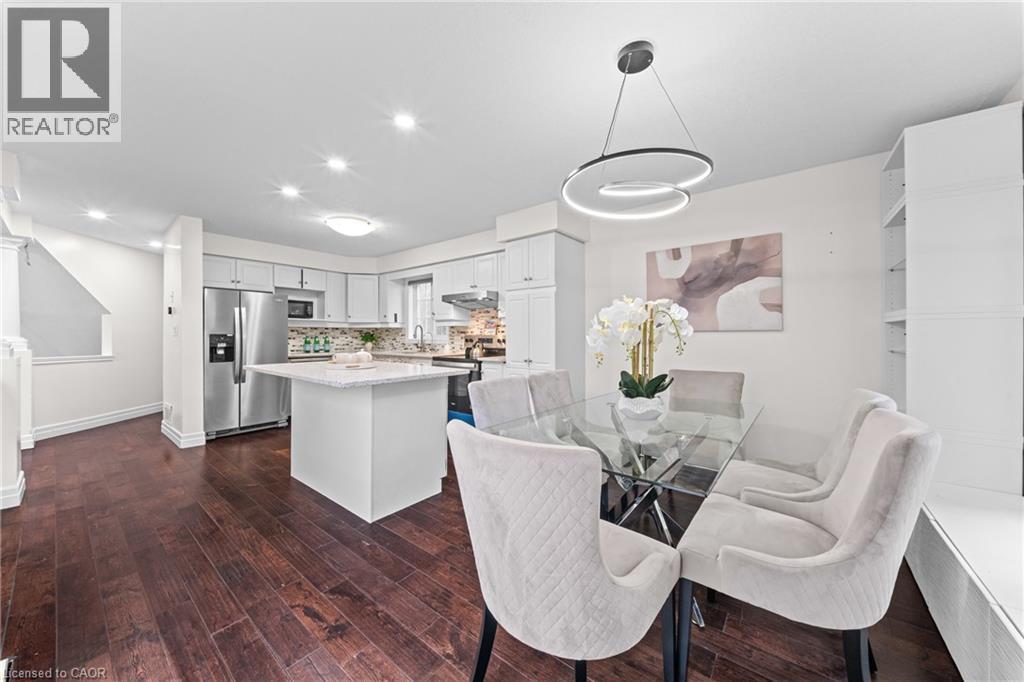 Dark wood-finish flooring throughout, white kitchen cabinetry with stainless steel appliances, and a kitchen island with a light-colored countertop - 495 Brigantine Drive, Waterloo, ON