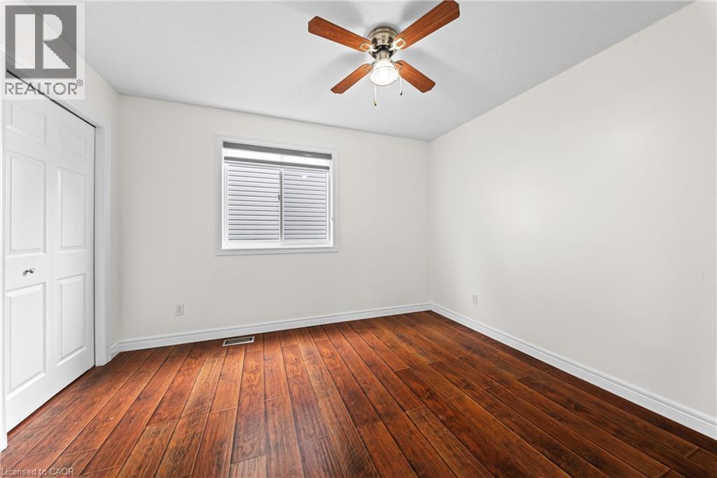 Wood-finish flooring with white trim, a double-door closet, a window with blinds, and a ceiling fan with light fixture - 495 Brigantine Drive, Waterloo, ON