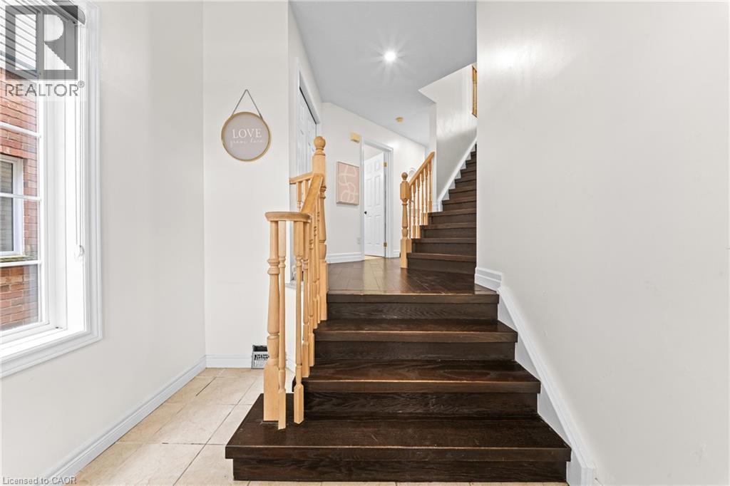 Dark wood-finish staircase with light wood railings, white walls, and ceramic tile flooring - 495 Brigantine Drive, Waterloo, ON