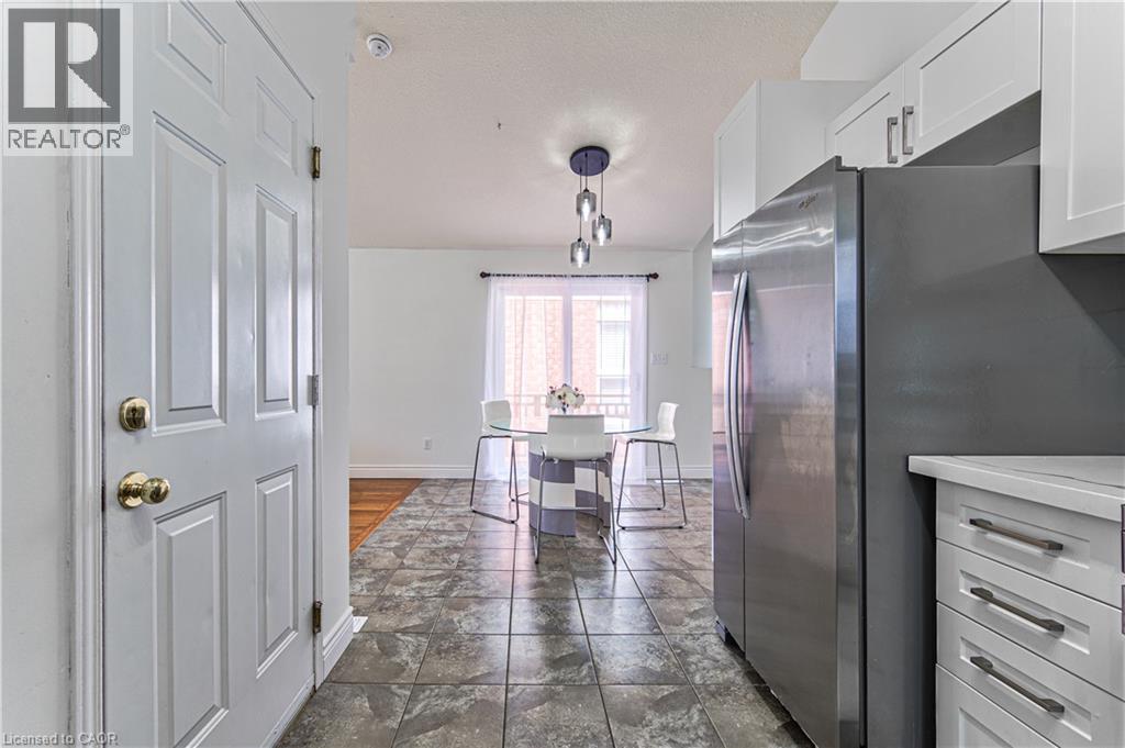 Tile flooring, white cabinetry, stainless steel refrigerator, white countertops, and modern pendant lighting - 168 Copper Leaf Street, Kitchener, ON