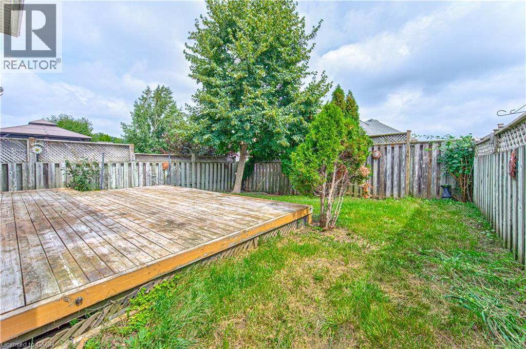 Expansive backyard featuring a wood deck, wood fencing, and mature trees - 168 Copper Leaf Street, Kitchener, ON