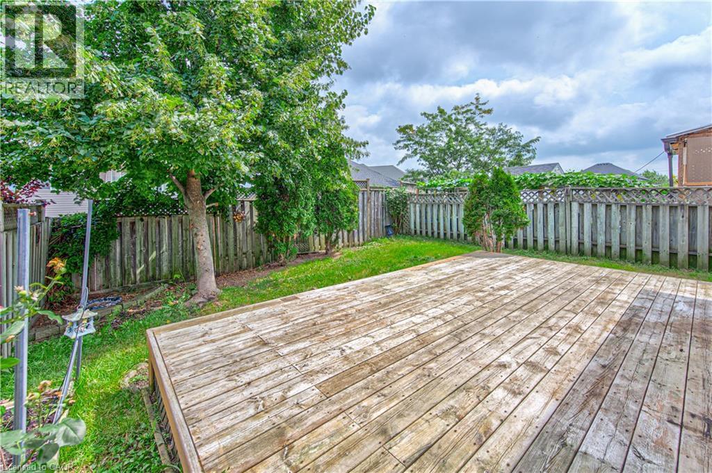 Expansive wood deck with surrounding green lawn, mature trees, and a wooden privacy fence - 168 Copper Leaf Street, Kitchener, ON